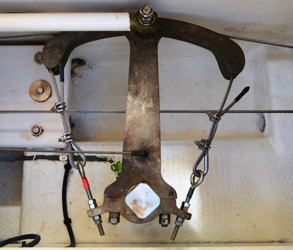 This steering quadrant clamps onto the rudder post at the bottom center. The round post has been machined square to accept an emergency tiller. This older system relies on stainless steering cables to move the rudder. The cables wrap around thimbles to protect them from wear and the bitter end section is called the dead end. 