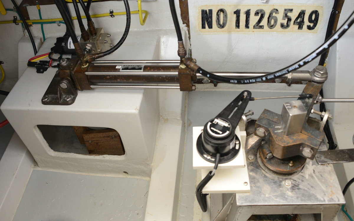 In this hydraulic steering arrangement, a pump (upper-left) drives a hydraulic piston that attaches to the tiller arm on the rudder post. Any accumulation of hydraulic fluid demands attention & corrosion on the ram will damage the piston seals. All attachments in this image should be checked for movement while executing hard turns.