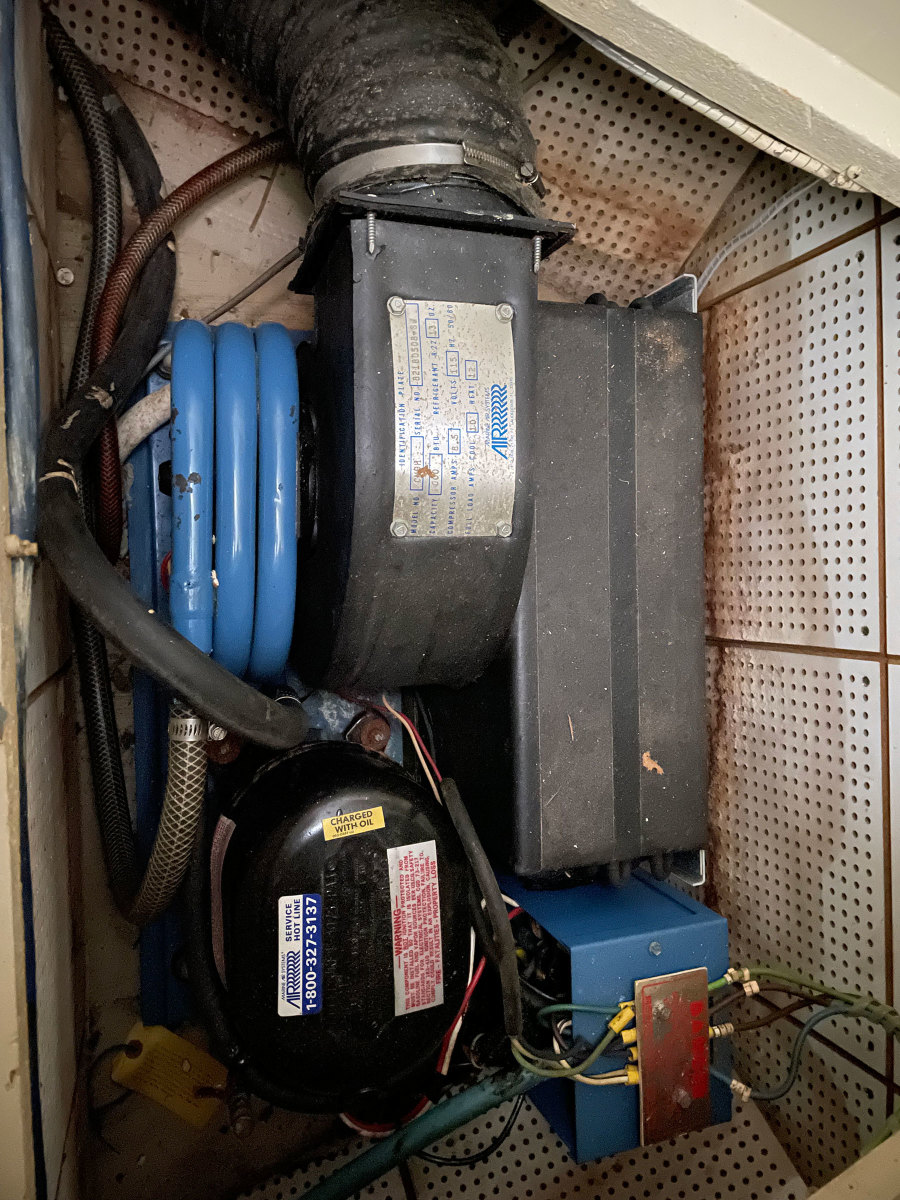 This self-contained air conditioning unit fits snugly under the V-berth, a common installation location. Note the vinyl drinking water hose connected to the blue coil, not approved for below-the-waterline use.