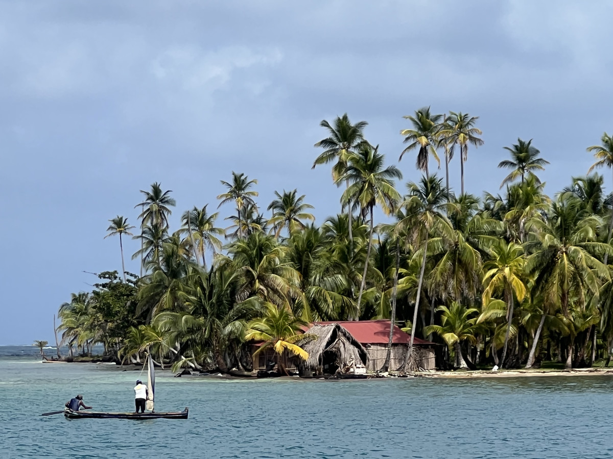 Two fishermen in a sail-rigged canoe visit a neighboring island, with traditional Kuna housing in the background.  